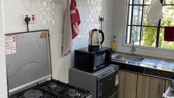 Une cuisine équipée d’une cuisinière à gaz, d’un four à micro-ondes et d’un réfrigérateur, avec des armoires en bois, une fenêtre offrant une belle vue et un dosseret carrelé.