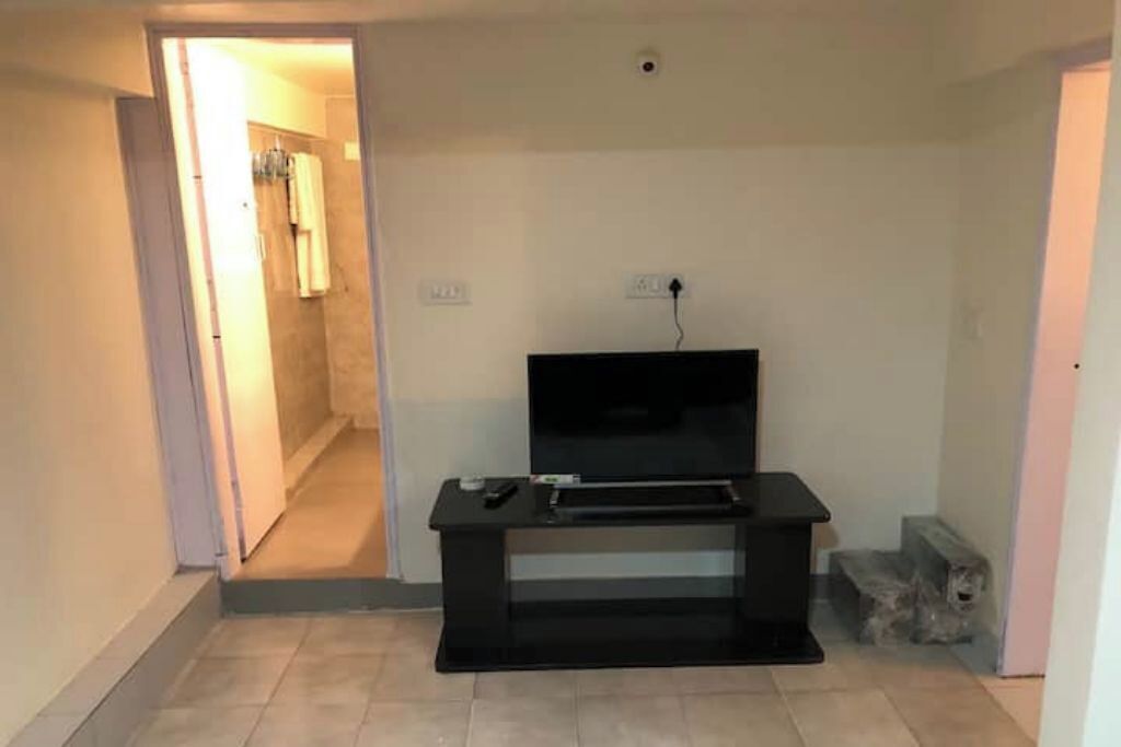 Een kamer met een zwarte entertainmentkast, een televisie en een stopcontact aan de muur.
