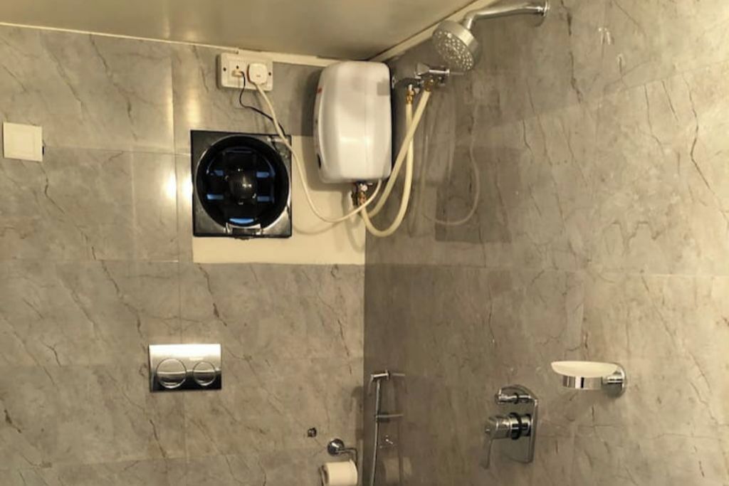 A bathroom with a marble wall, a built-in heater, a handheld showerhead, a toilet paper holder, and a soap dish.