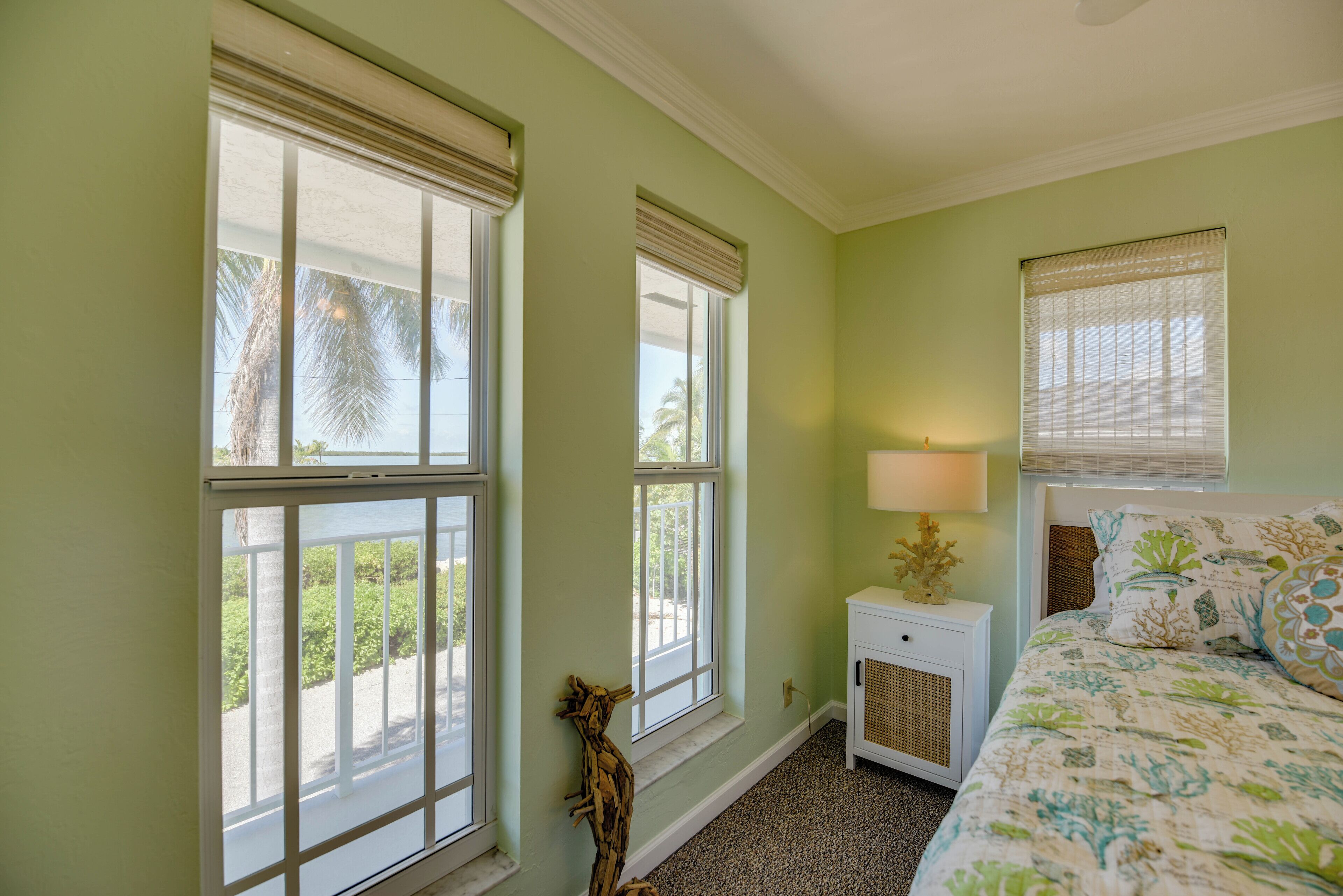 A bedroom with large windows, a bedside table with a lamp, and a bed with floral bedding.