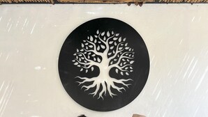 Una pareja sentada en un sofá con un cuadro grande de un árbol en la pared detrás, dos mesitas de madera con pasteles y un piso de concreto.