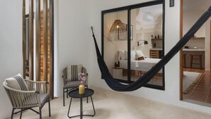 Una habitación acogedora con una hamaca, una silla de mimbre, una mesita redonda y una cama con un ventanal grande.