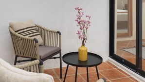 Un patio en esquina con mobiliario de mimbre, una mesita redonda con un jarrón de flores y dos ventanas.