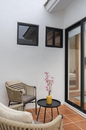 Un patio en esquina con mobiliario de mimbre, una mesita redonda con un jarrón de flores y dos ventanas.