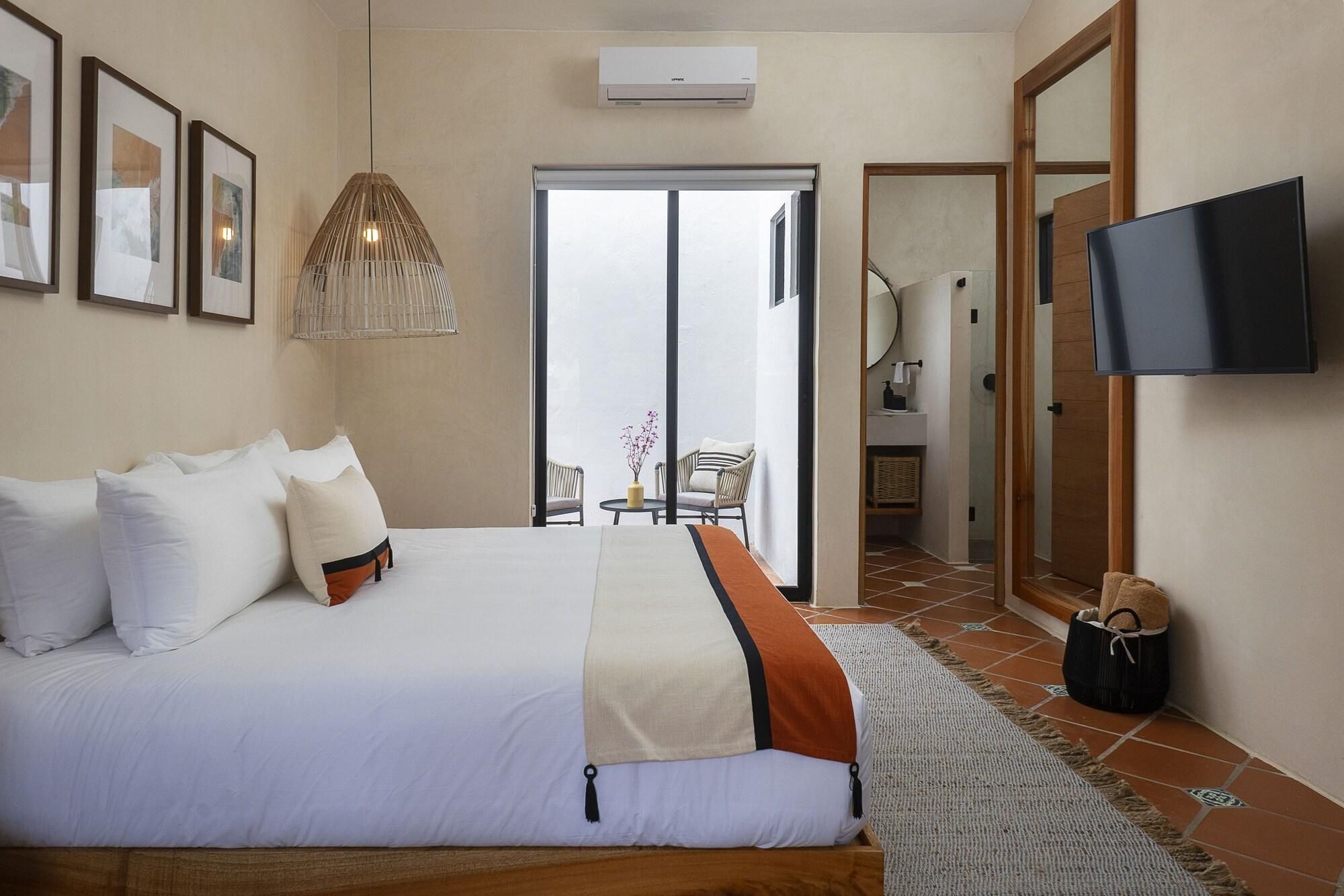 A hotel room with a bed, a TV, a door leading to a bathroom, and a view through a glass door.
