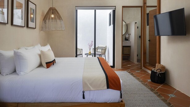 Habitación de hotel con cama, televisor, puerta que da a un baño y vistas a través de un ventanal.