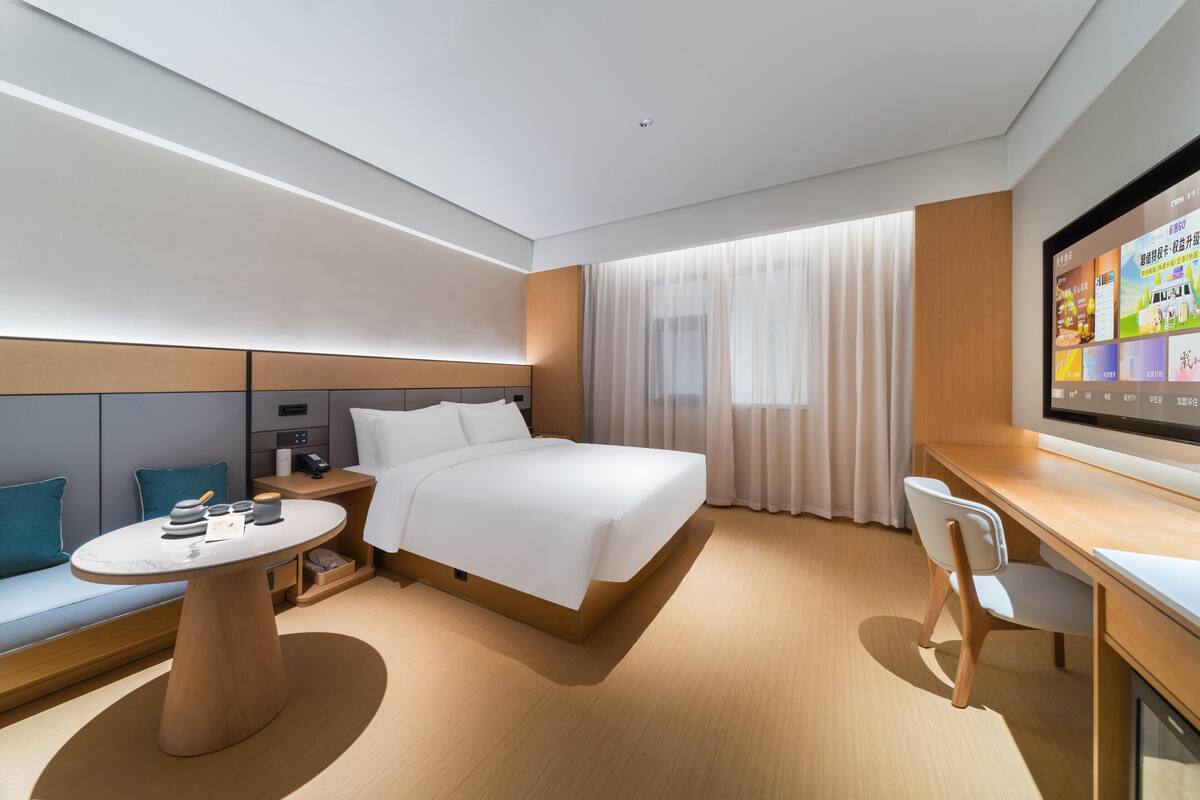 Une chambre d’hôtel moderne équipée d’un lit, d’un bureau, d’une chaise, d’une petite table et d’un téléviseur.