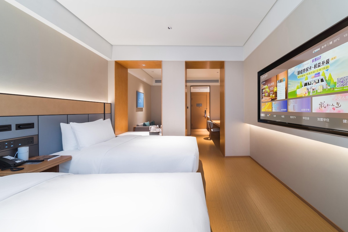 Une chambre d’hôtel avec deux lits, un bureau avec un téléphone et un téléviseur fixé au mur.