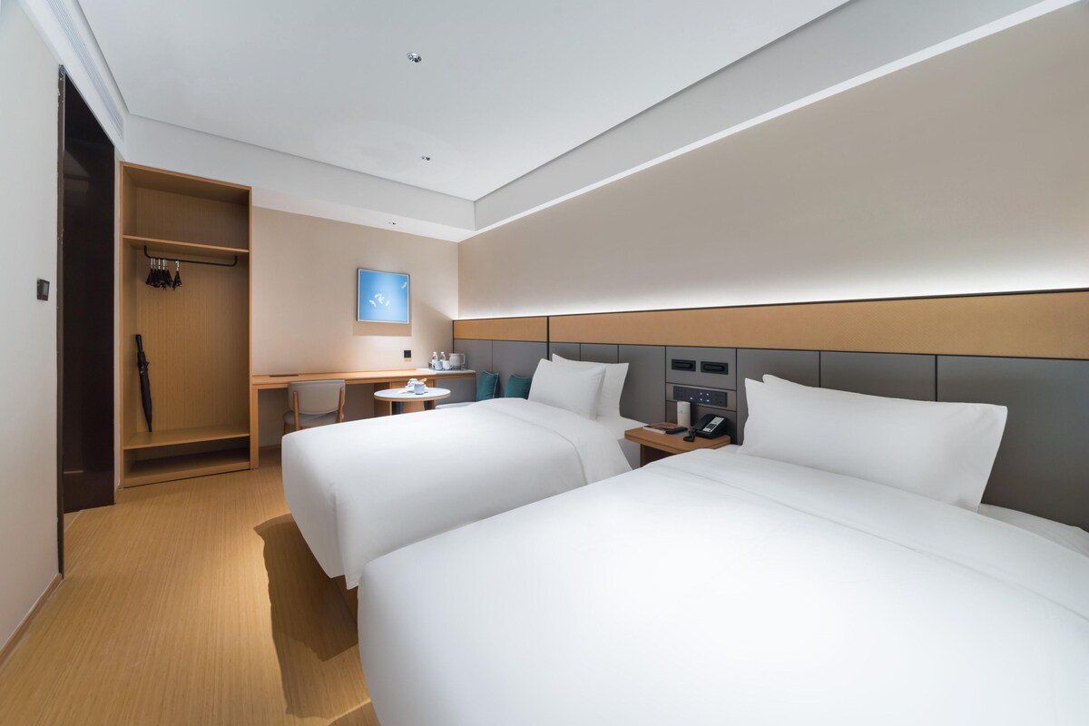 A hotel room with two beds, a desk, a chair, a wardrobe, and a bedside table with a phone.