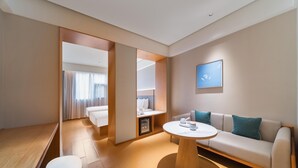 A modern hotel room with a sofa, a round coffee table, and a bed with a nightstand.