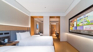 A hotel room with two beds, a TV mounted on the wall, a desk with a phone, and a small table with a lamp.