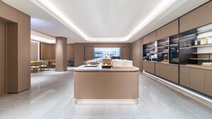 A modern hotel lobby with a central reception desk, seating area, and a large window providing a view of the city.