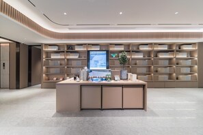Uma área de recepção moderna com um balcão central, um visor digital e uma estante cheia de livros e objetos decorativos.