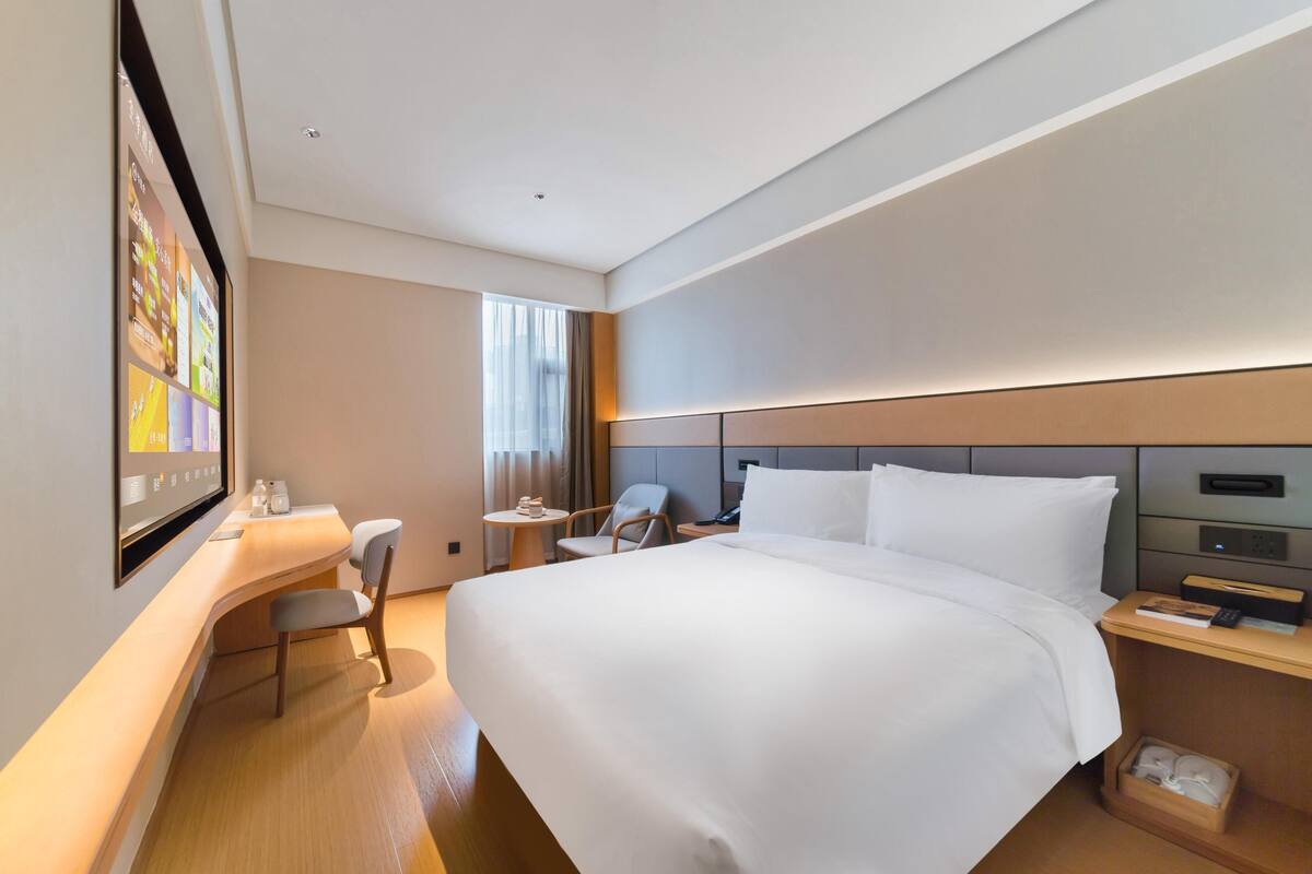 Une chambre d’hôtel moderne équipée d’un grand lit, d’un bureau avec une chaise, d’une petite table et d’un téléviseur fixé au mur.