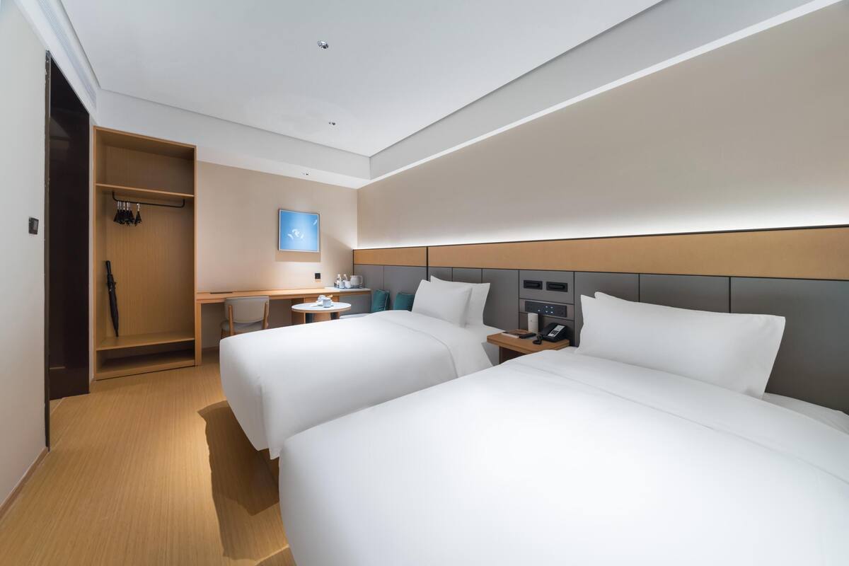 Une chambre d’hôtel avec deux lits, un bureau, une chaise, une armoire et une table de chevet avec un téléphone.