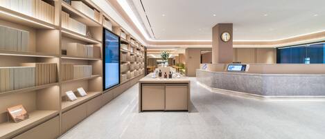 Una moderna hall d'albergo con una reception, un grande schermo digitale e una ben fornita libreria.