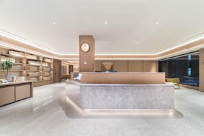 A modern hotel reception area with a marble counter, a large plant, and a seating area with a green chair. - Ji Hotel Guangzhou Caihongqiao Metro Station (Guangzhou)