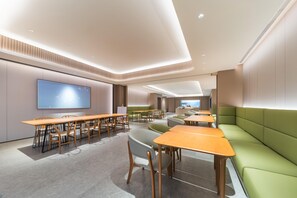 Ein moderner Konferenzraum mit mehreren Tischen und Stühlen, einem großen Flachbildfernseher und einer grünen Lounge-Ecke.