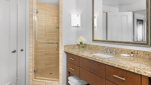 A bathroom with a shower, a sink, a mirror, and a vanity with drawers.