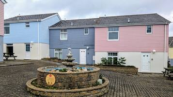 A courtyard with a stone fountain, a picnic table, and colorful houses.
