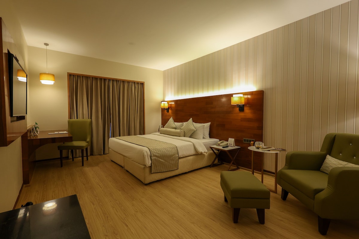 A hotel room with a large bed, a desk, a chair, a sofa, and a small table.