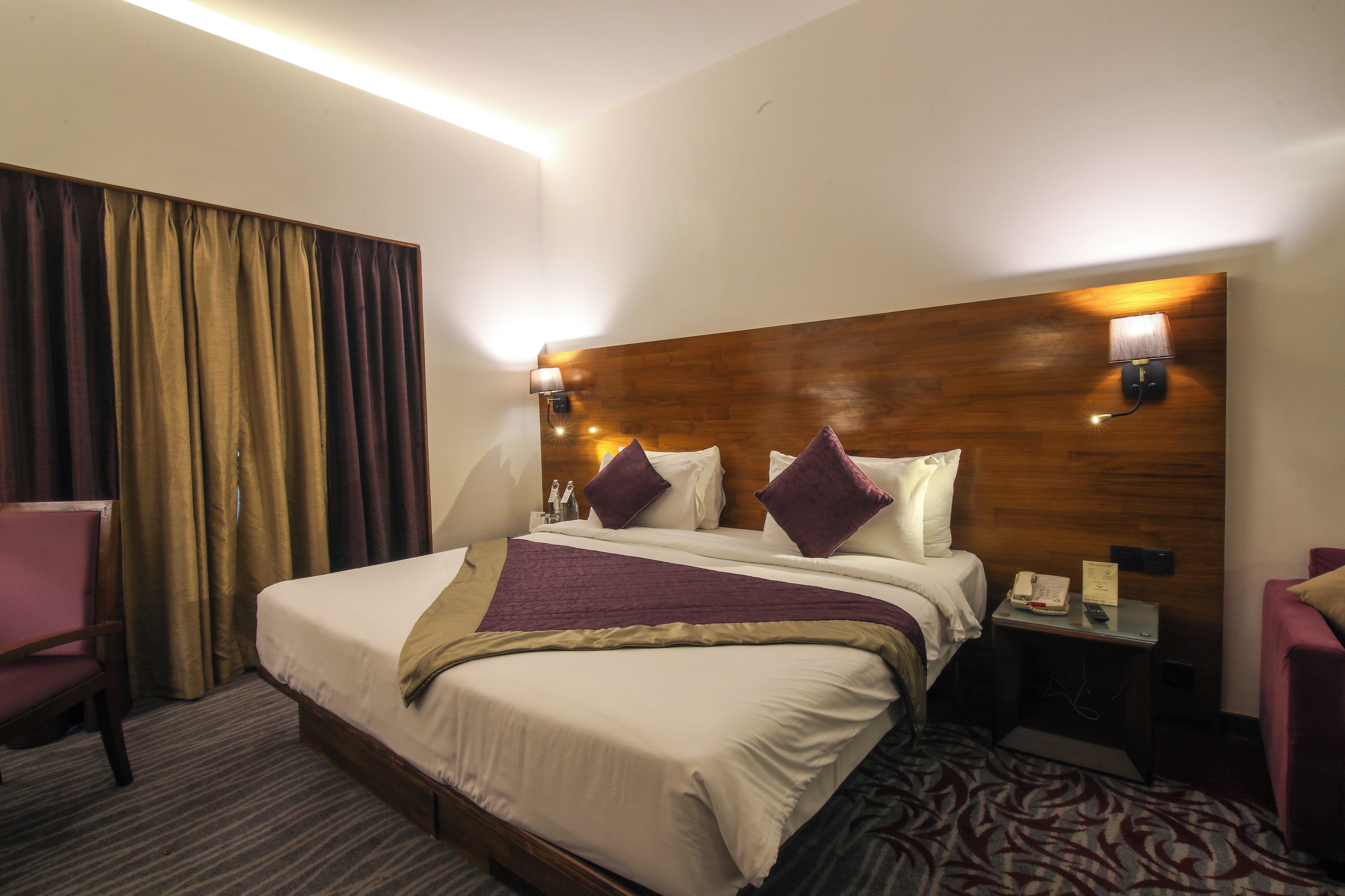 Habitación de hotel con una cama grande, dos lámparas de noche, cabecera de madera, un escritorio con teléfono y una silla.
