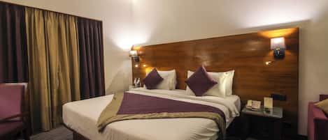 Habitación de hotel con una cama grande, dos lámparas de noche, cabecera de madera, un escritorio con teléfono y una silla.