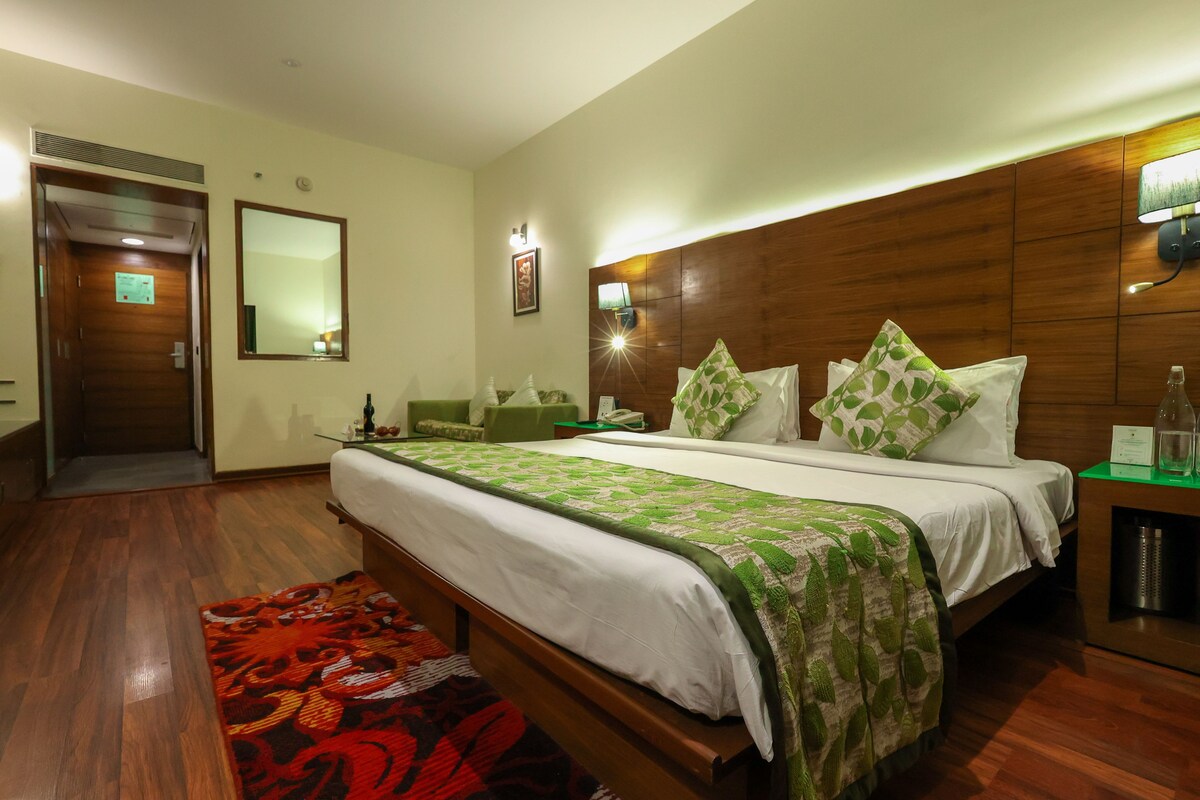 A hotel room with a large bed, a wooden headboard, a nightstand, a mirror, and a red patterned rug.