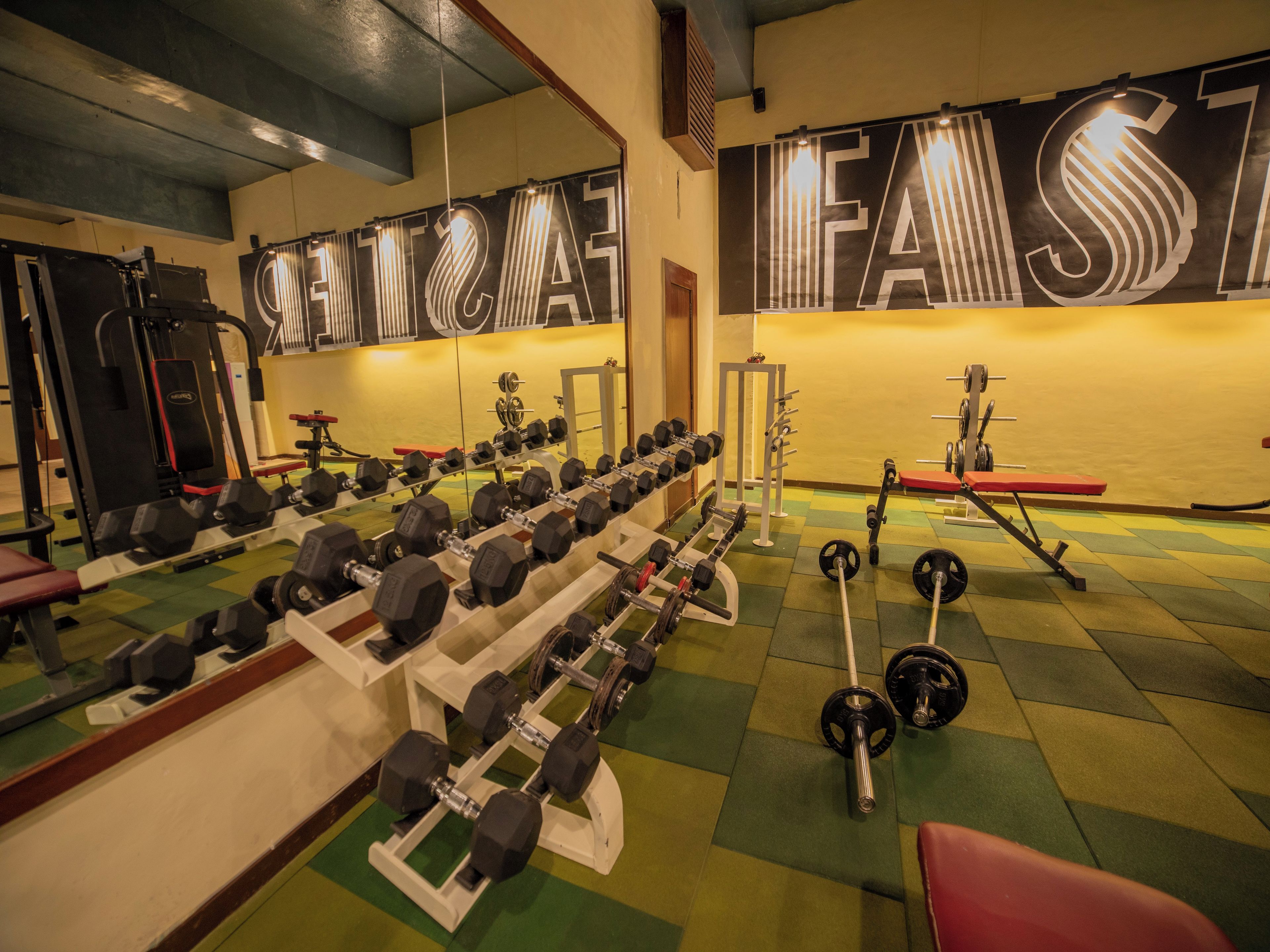 Un gimnasio con diverso equipo de ejercicio, incluyendo mancuernas y máquinas de pesas, dispuesto de forma ordenada.