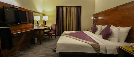 Una habitación de hotel con una cama, un escritorio con televisor, dos lámparas y una cortina.