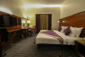 A hotel room with a bed, a desk with a television, two lamps, and a curtain. - The Orchid Hotel, Pune (Pune)