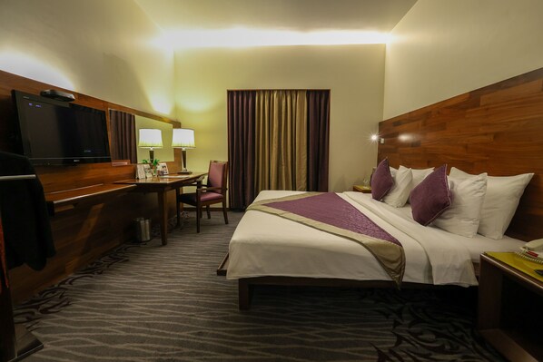 A hotel room with a bed, a desk with a television, two lamps, and a curtain. - The Orchid Hotel, Pune (Pune)