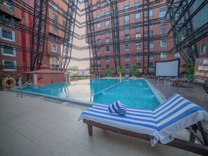 A swimming pool with a lounge chair and a towel, surrounded by a building with a red brick facade and black scaffolding. - The Orchid Hotel, Pune (Pune)