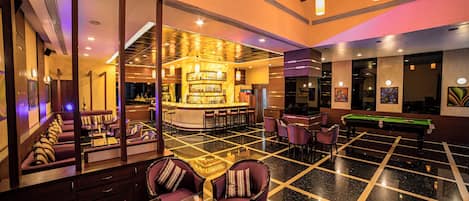 Un vestíbulo de hotel con zona de bar, asientos y mesa de billar.