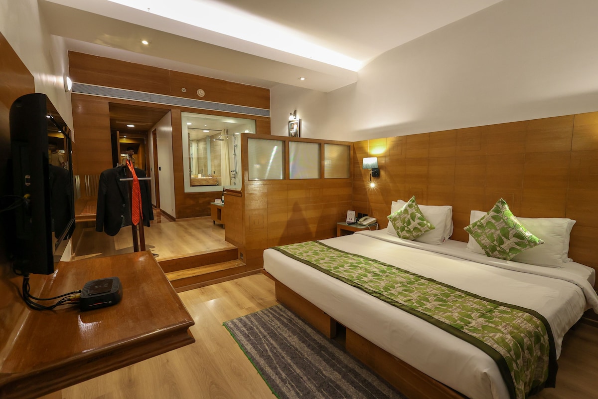 A hotel room with a large bed, a bedside table with a phone, a mirror, and a wooden wardrobe.