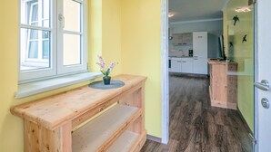 A wooden bench with a potted plant, a window, and a view into a kitchen area with cabinets and a refrigerator. - Ferienwohnun Stainz 4 Personen (Stainz)