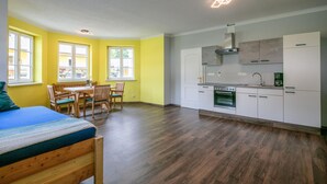 A compact apartment with a kitchenette, a dining area with a table and chairs, and a bed with a blue cover. - Ferienwohnun Stainz 4 Personen (Stainz)