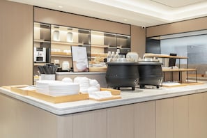 Un espace cuisine moderne comprenant un coin café, un buffet et un grand appareil noir, probablement un robot culinaire ou un mixeur.