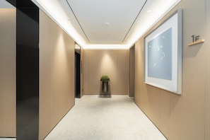 Un couloir moderne au design minimaliste, avec un revêtement de sol de couleur claire, des murs en bois et une œuvre d’art encadrée sur le mur de droite.