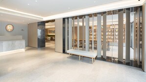 Un hall d’hôtel moderne avec un comptoir d’accueil, un banc et une vue sur un espace bibliothèque bien éclairé.