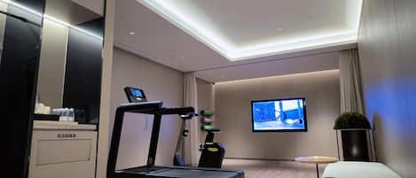 A modern hotel room with a treadmill, a television, and a small table.