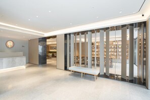 Eine moderne Hotelhalle mit einer Rezeption, einer Sitzbank und Blick in einen gut beleuchteten Bibliotheksbereich.