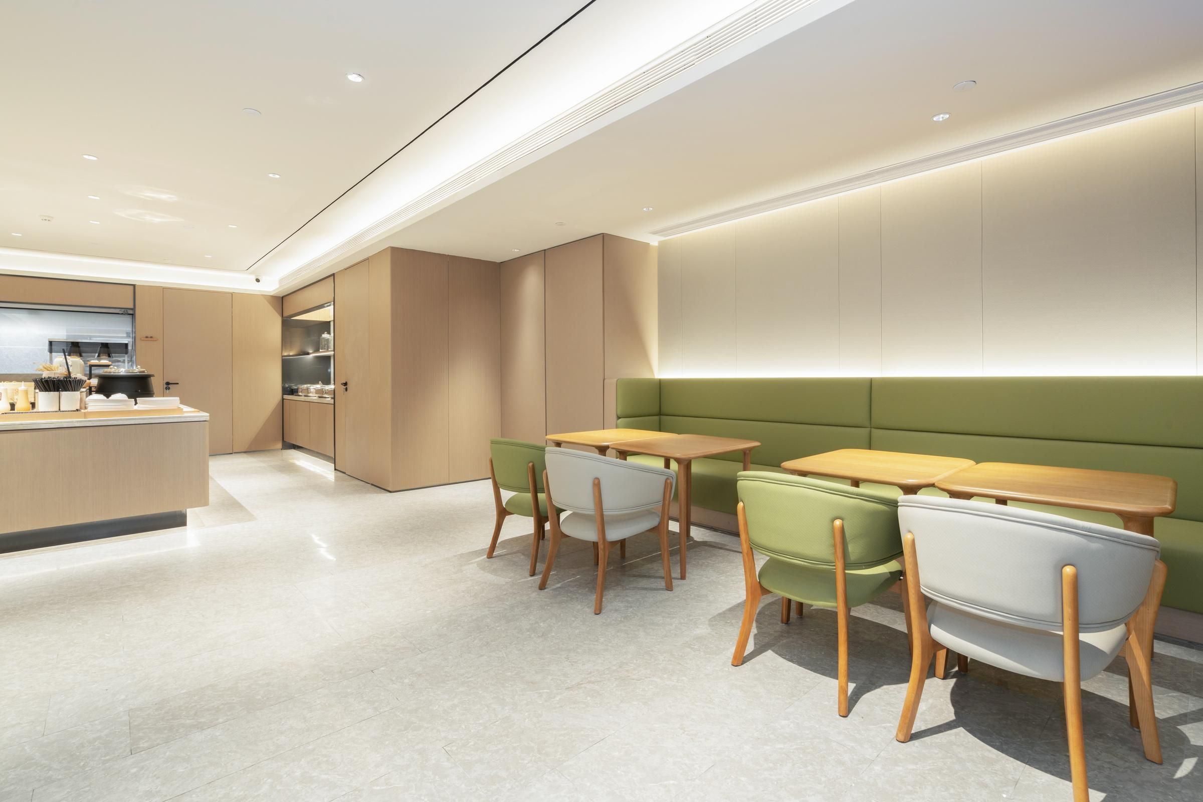 A modern kitchen with a central island, wooden tables, and green chairs.