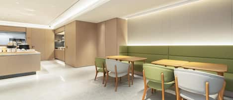 A modern kitchen with a central island, wooden tables, and green chairs.