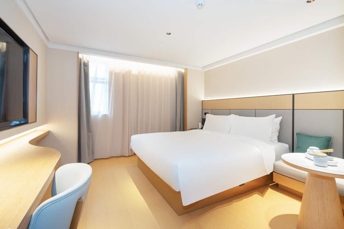 Una habitación de hotel moderna con una cama grande, un escritorio y una mesa redonda.