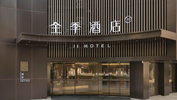Une entrée d’hôtel moderne, avec une enseigne bien visible en caractères chinois et le mot « HÔTEL » en anglais.