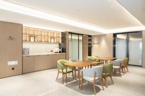 A modern kitchen with built-in appliances, a dining area with wooden tables and chairs, and a glass partition wall. - Ji Hotel Guangzhou Jiangtai Road Metro Station (Guangzhou)