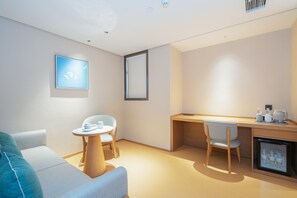A modern, minimalist room with a sofa, a small round table, a desk with a chair, and a mini-fridge. - Ji Hotel Guangzhou Jiangtai Road Metro Station (Guangzhou)