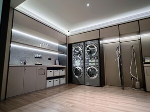 Une buanderie moderne équipée de machines à laver et de sèche-linge encastrés, d’une douche et d’armoires de rangement.