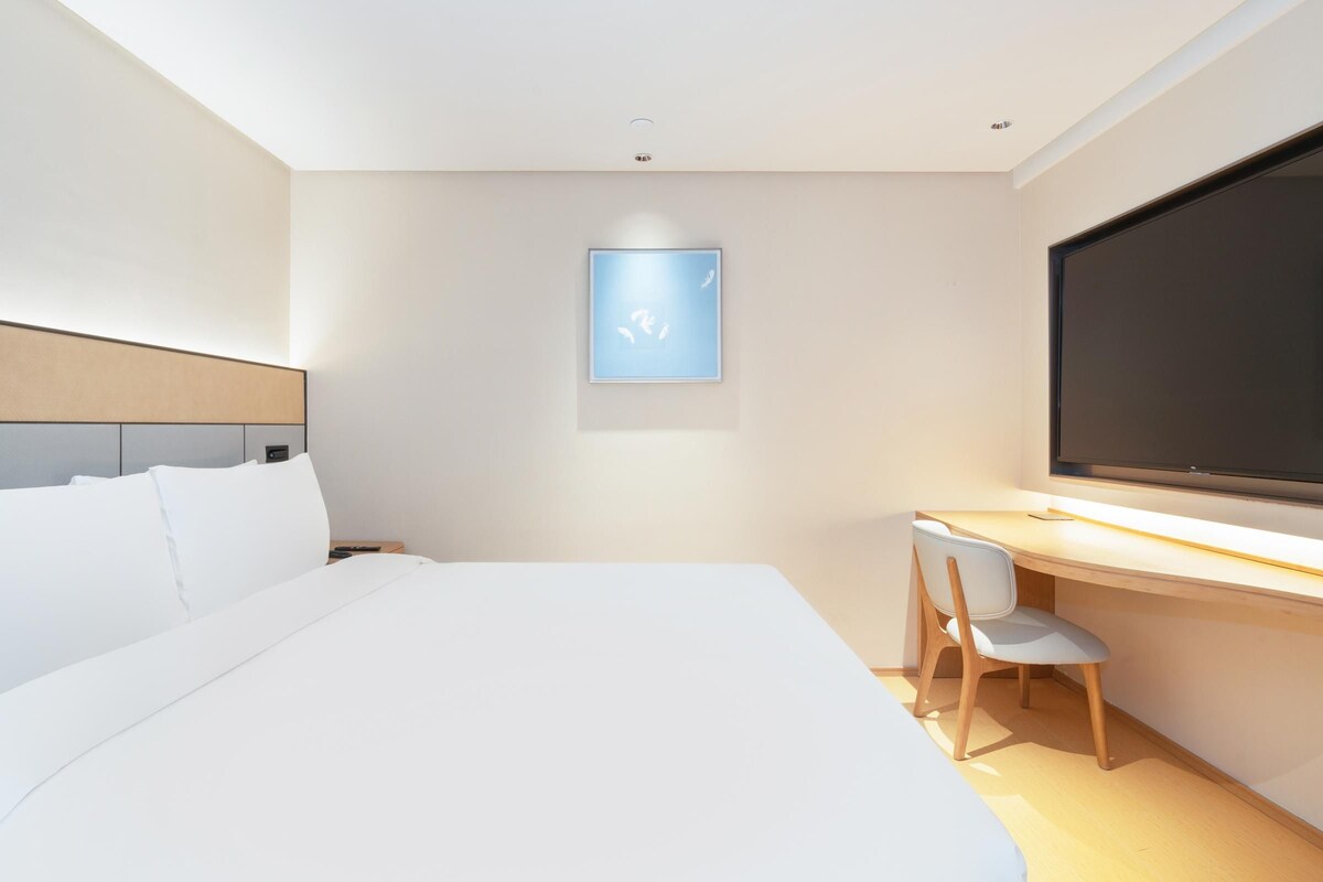 A modern hotel room with a large bed, a desk, and a TV.